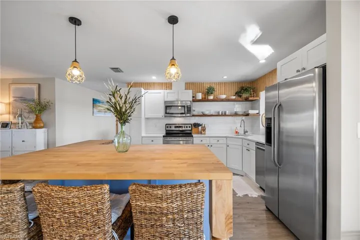 Kitchen with decorative backsplash, stainless steel appliances, sink, decorative light fixtures, and white cabinets