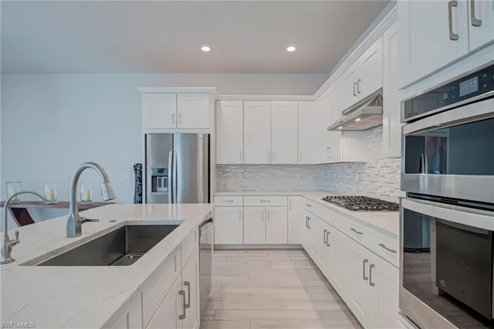 Kitchen with stainless steel appliances, white cabinets, tasteful backsplash, and recessed lighting