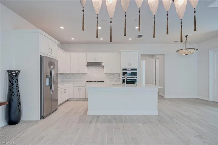 Kitchen featuring stainless steel appliances, white cabinets, backsplash, light wood finished floors, and pendant lighting