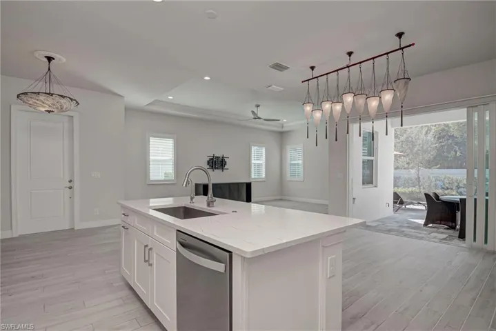 Kitchen featuring open floor plan, a tray ceiling, hanging light fixtures, white cabinets, and light stone countertops