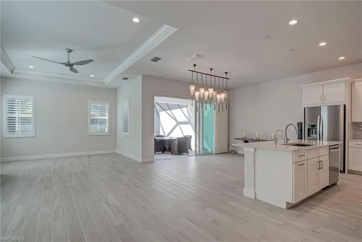 Kitchen featuring white cabinetry, open floor plan, an island with sink, a ceiling fan, and stainless steel appliances