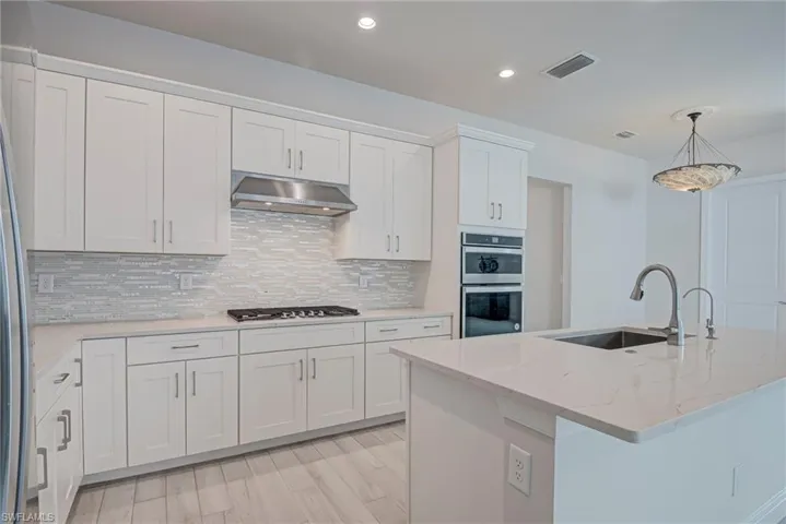 Kitchen featuring white cabinetry, light stone counters, light wood-style floors, stainless steel appliances