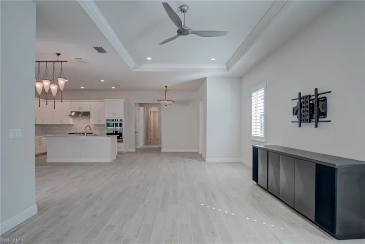 living room with hanging lights, light wood finished floors, a ceiling fan, crown molding, and a raised ceiling