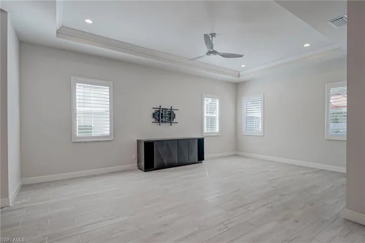 Living room featuring a raised ceiling, light wood-type flooring, a ceiling fan, recessed lighting, and ornamental molding