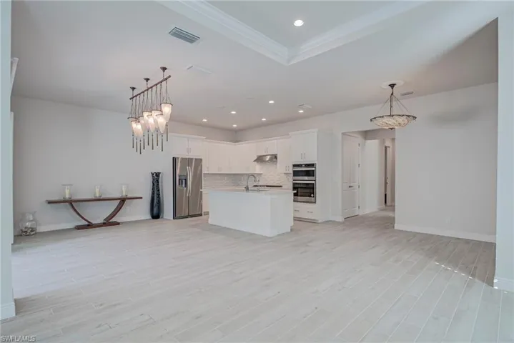 Kitchen with open floor plan, tasteful backsplash, white cabinetry, stainless steel appliances, and a center island with sink