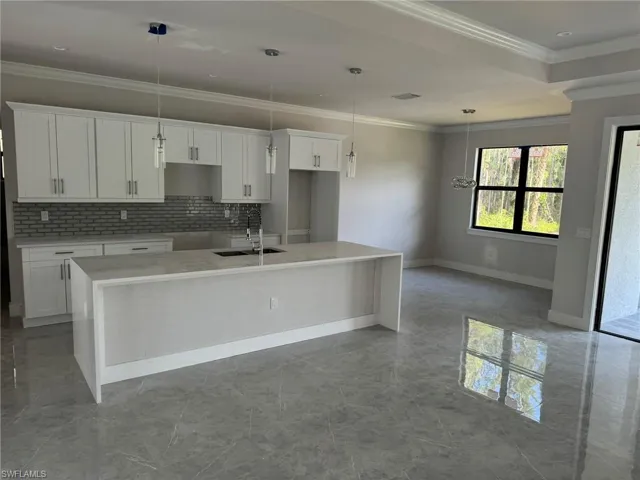 Kitchen featuring sink, decorative light fixtures, white cabinetry, and a kitchen island with sink