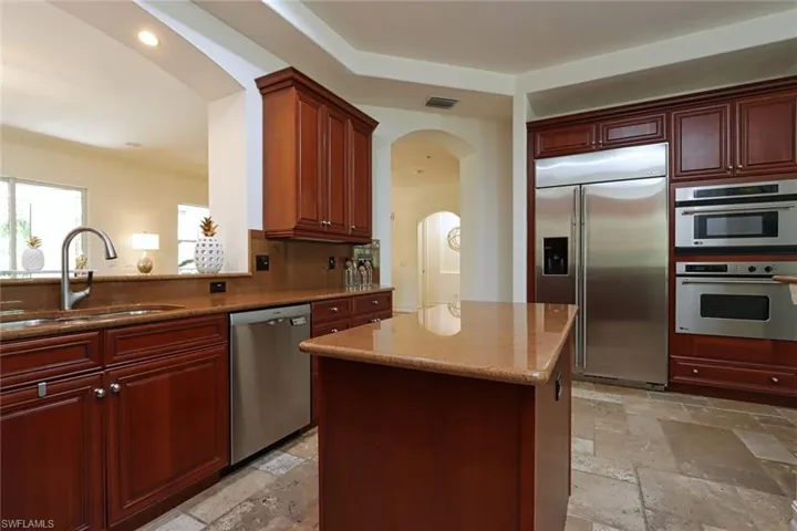 Kitchen with appliances with stainless steel finishes, stone tile flooring, arched walkways, light stone countertops, and recessed lighting