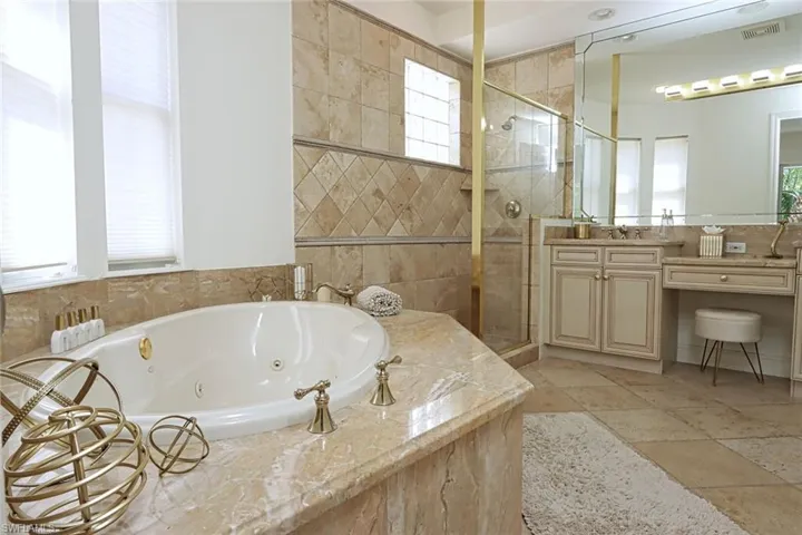 Full bathroom featuring a stall shower, vanity, a whirlpool tub, and stone tile flooring