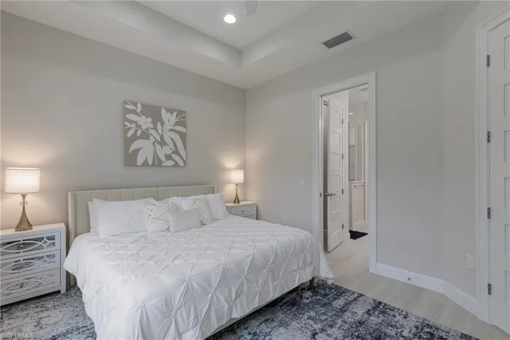 Bedroom featuring light wood finished floors, recessed lighting, ensuite bath, a ceiling fan, and a raised ceiling