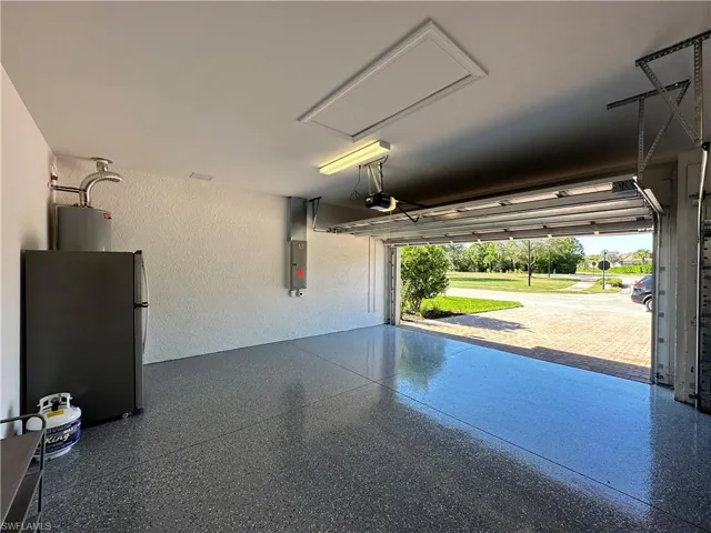 Garage featuring a textured wall, freestanding refrigerator, electric panel, and water heater
