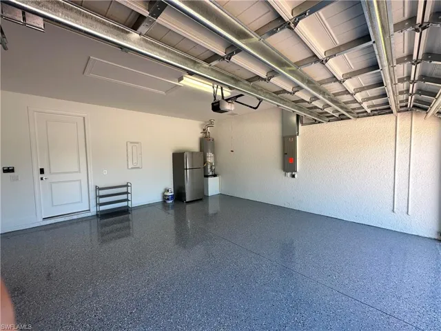 Garage with freestanding refrigerator, electric panel, and water heater