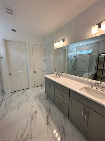 Full bath featuring light marble finish flooring, a marble finish shower, and double vanity