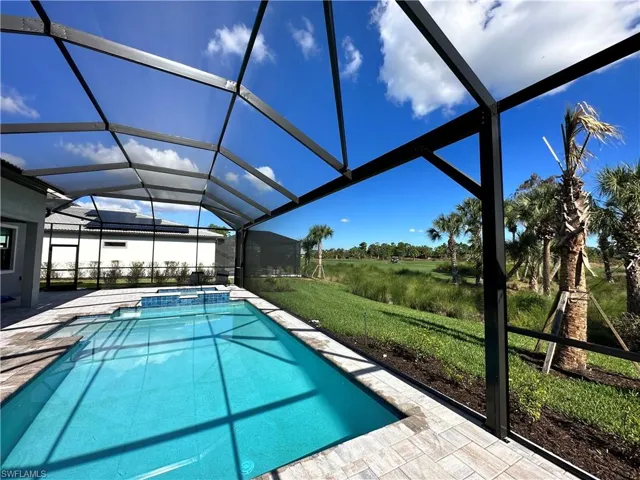 View of swimming pool featuring glass enclosure, a pool with connected hot tub, a patio, a sunroom, and a lawn