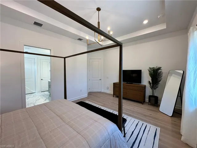 Bedroom with light wood finished floors, a chandelier, recessed lighting, and a raised ceiling