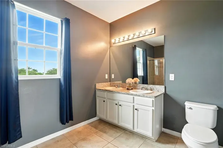 Bathroom with plenty of natural light, double vanity, light tile patterned flooring, and a stall shower