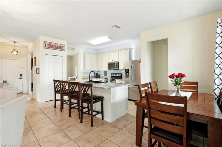 Kitchen with a center island with sink, stainless steel appliances, white cabinets, light stone countertops, and light tile patterned floors