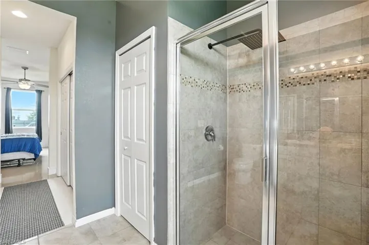 Ensuite bathroom with a stall shower, tile patterned floors, ceiling fan, and a closet
