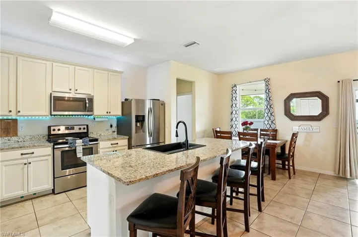 Kitchen featuring appliances with stainless steel finishes, cream cabinetry, a breakfast bar, and light stone countertops