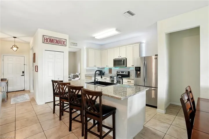 Kitchen featuring appliances with stainless steel finishes, light stone counters, light tile patterned floors, and an island with sink