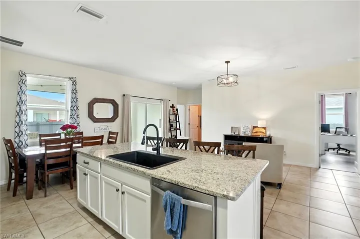 Kitchen featuring healthy amount of natural light, stainless steel dishwasher, an island with sink, and white cabinets
