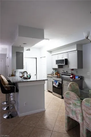Kitchen with dark stone counters, stainless steel appliances, a breakfast bar area, and light tile patterned flooring