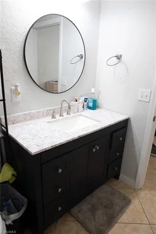 Bathroom with a textured wall, vanity, and light tile patterned flooring