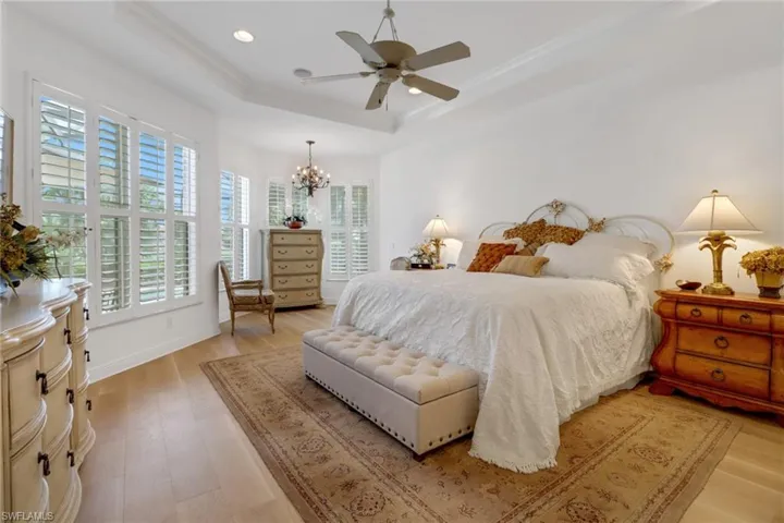 Bedroom featuring ceiling fan with notable chandelier, ornamental molding, light hardwood / wood-style floors, and a tray ceiling