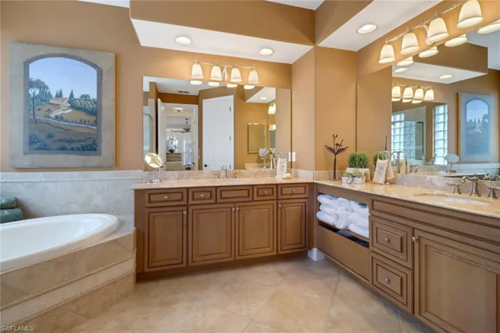 Bathroom featuring tiled tub, vanity, and tile patterned flooring
