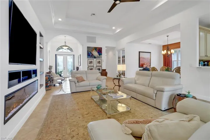 Living room with light tile patterned floors, a raised ceiling, ceiling fan with notable chandelier, and built in shelves