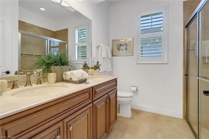 Bathroom with an enclosed shower, double vanity, toilet, and tile patterned flooring
