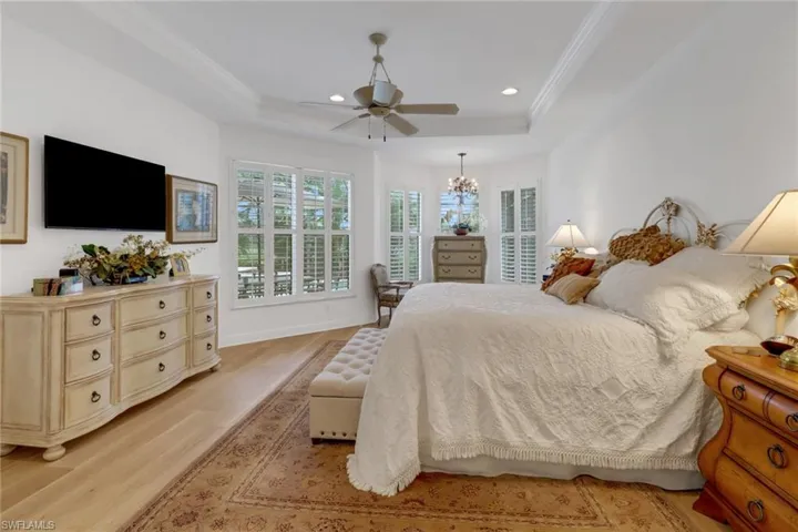 Bedroom featuring light hardwood / wood-style flooring, ceiling fan with notable chandelier, crown molding, and a raised ceiling