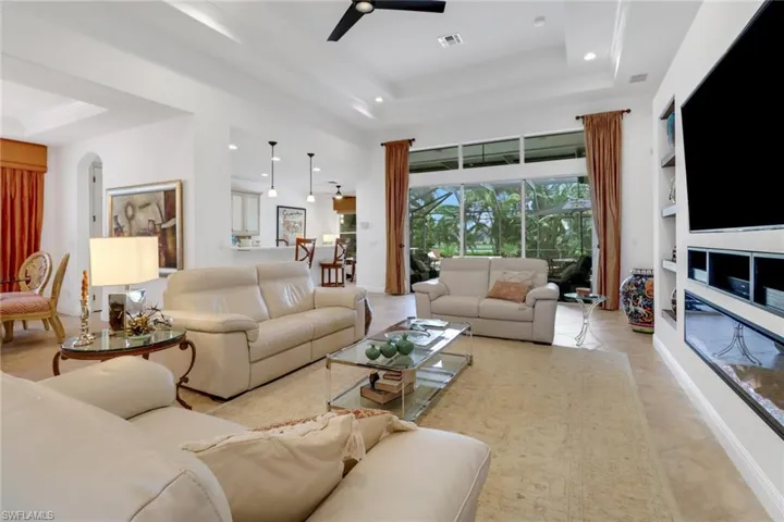 Living room featuring ceiling fan, light tile patterned flooring, built in features, and a tray ceiling