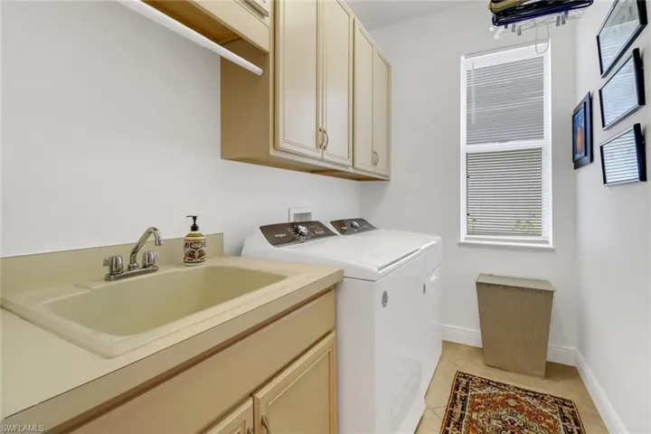 Washroom with sink, washing machine and dryer, cabinets, and light tile patterned flooring
