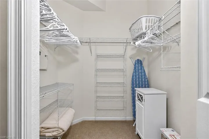 Organized closet space featuring wire shelving systems, multiple hanging rods, and neutral carpet flooring