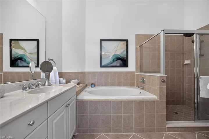 Bathroom featuring a built-in jetted tub, a glass-enclosed shower, a double vanity with a light-toned countertop, and tiled flooring