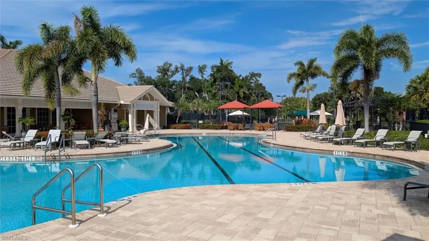 Resort-style swimming pool featuring a curved design, paved sundeck, and lush tropical landscaping