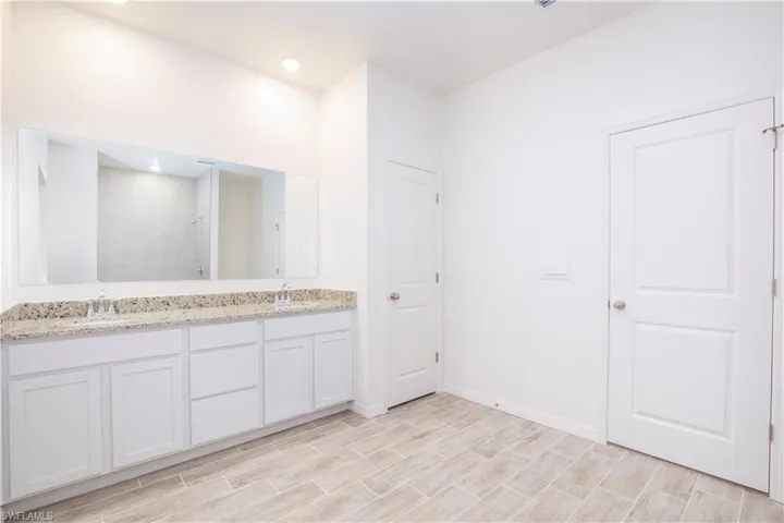 Full bathroom with double vanity, a walk in shower, and wood finish floors