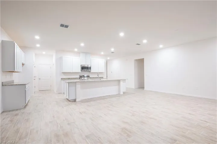 Kitchen with white cabinets, light wood-style flooring, stainless steel appliances, a kitchen island with sink, and recessed lighting
