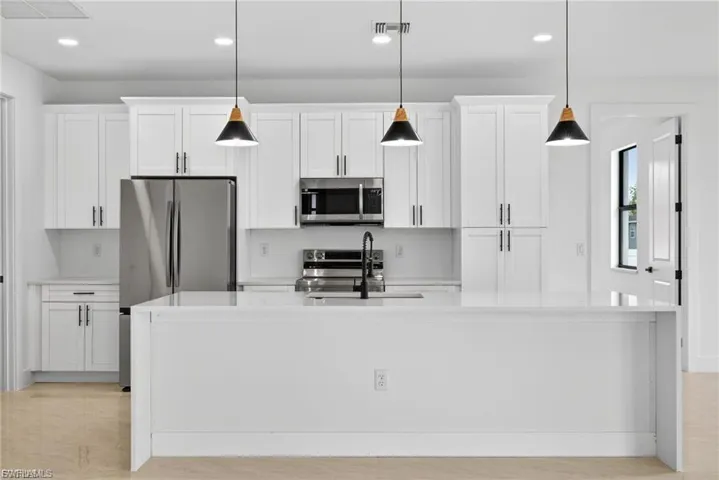 Kitchen with a center island with sink, white cabinets, stainless steel appliances, light stone counters, and decorative light fixtures