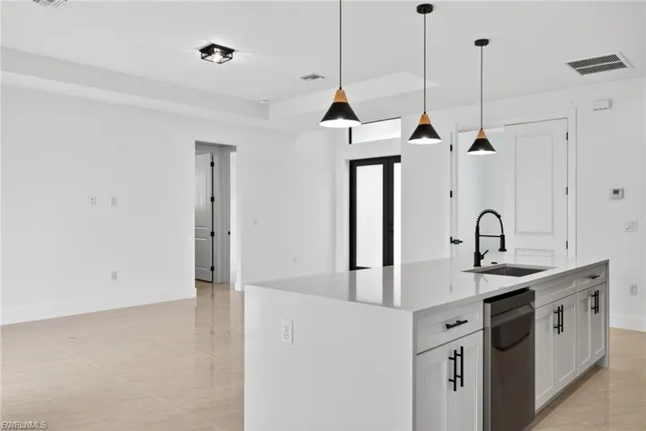 Kitchen with a kitchen island with sink, light stone counters, hanging light fixtures, white cabinets, and a tray ceiling