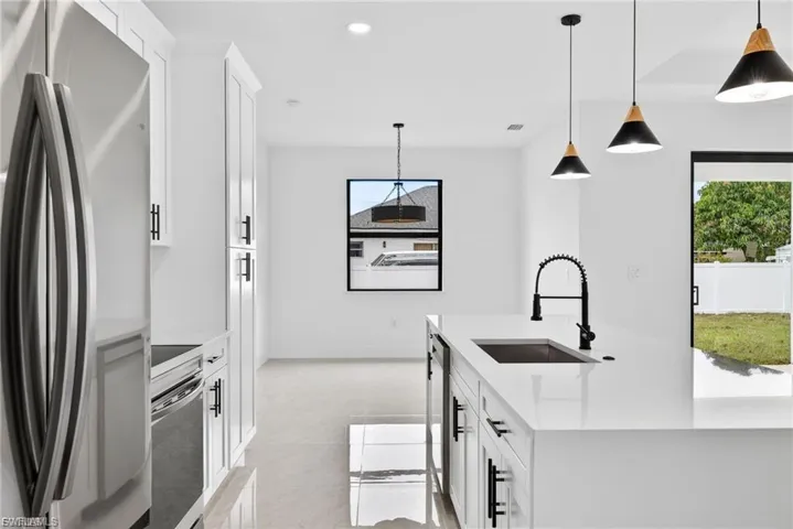 Kitchen with stainless steel appliances, a center island with sink, white cabinets, light stone countertops, and pendant lighting