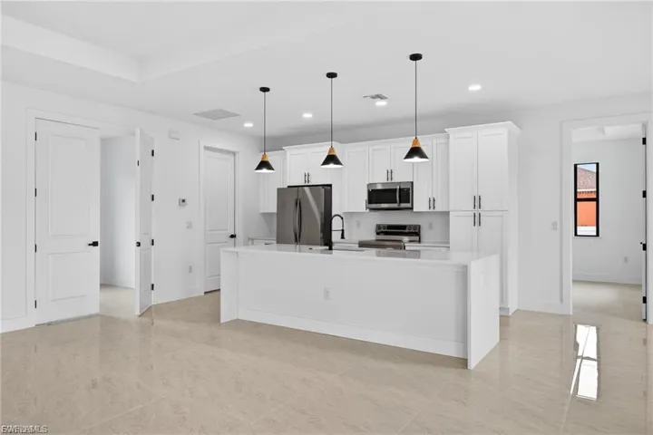 Kitchen featuring white cabinetry, an island with sink, stainless steel appliances, decorative light fixtures, and light stone counters