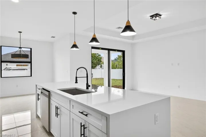 Kitchen featuring an island with sink, light stone counters, pendant lighting, white cabinetry, and light tile patterned floors