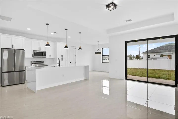 Kitchen with stainless steel appliances, white cabinets, a kitchen island with sink, a raised ceiling, and hanging light fixtures