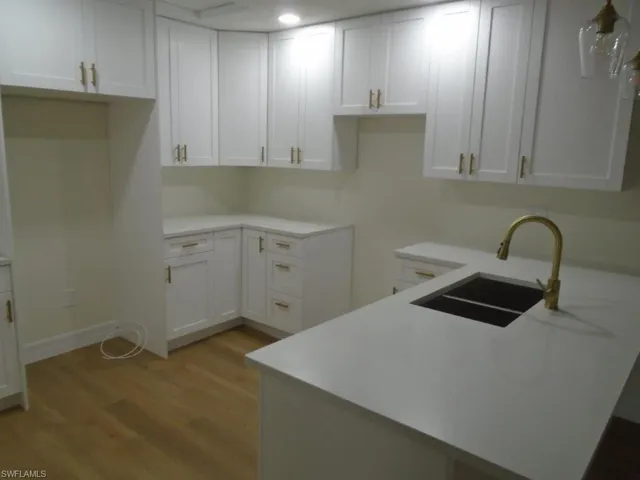 Kitchen with white cabinets, sink, light hardwood / wood-style floors, and kitchen peninsula