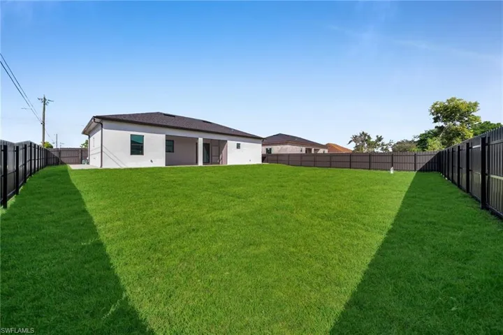 Backyard featuring an expansive lawn, neutral stucco exterior, covered rear patio, and full-perimeter privacy fencing