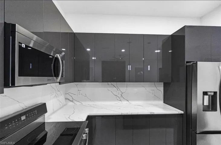 Kitchen featuring light stone countertops, modern cabinets, stainless steel appliances, and dark cabinetry