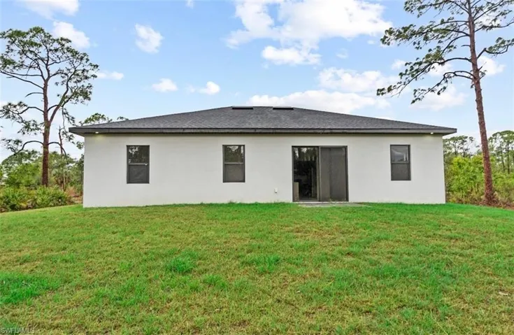 Back of property with a yard, stucco siding, and a shingled roof