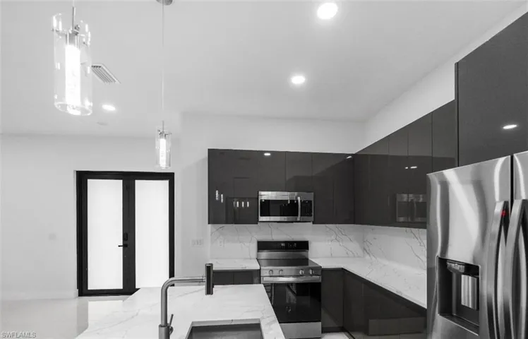 Kitchen with dark cabinets, modern cabinets, stainless steel appliances, light stone countertops, and pendant lighting