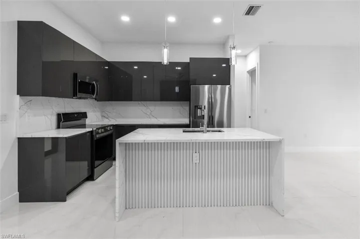 Kitchen featuring dark cabinets, stainless steel appliances, a center island with sink, and light stone counters